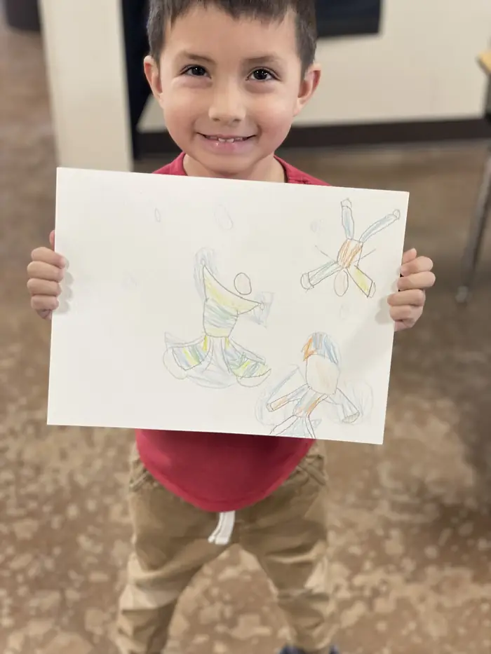 A young Cornerstone student smiling and holding up his coloured-pencil drawing