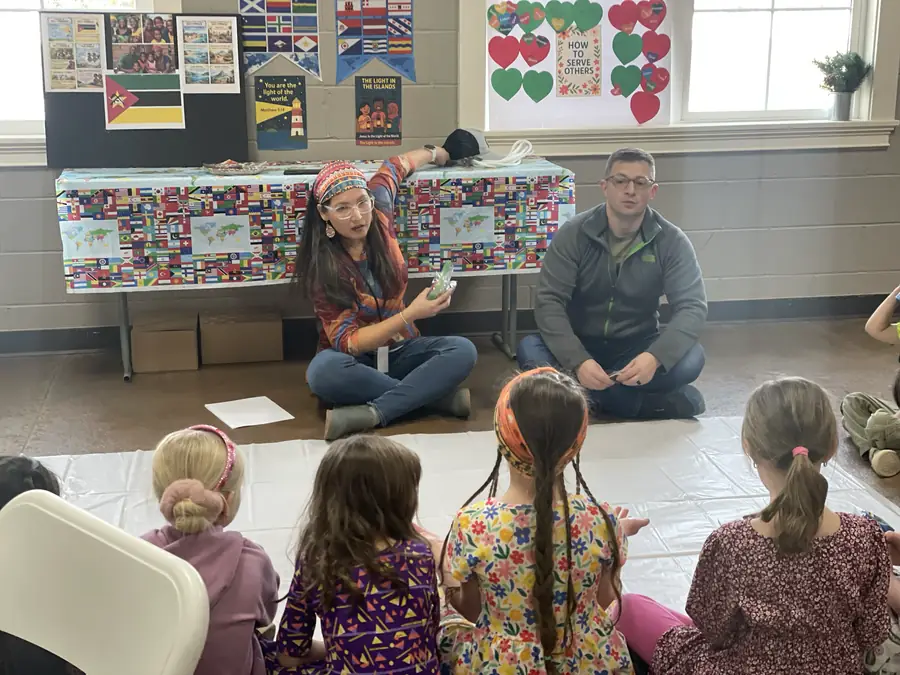 Cornerstone Community Schoolhouse students sitting on the floor for a lesson in front of a table covered in world flags