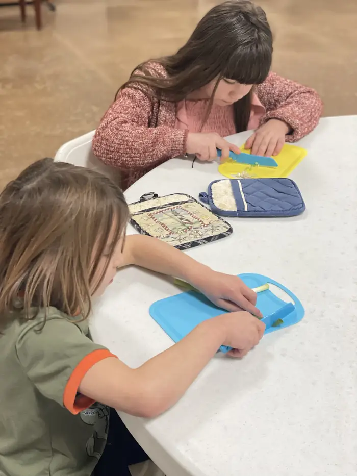 Two Cornerstone students chopping green onions with child-safe knives in a cooking lesson