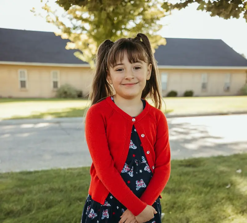 A Cornerstone Community Schoolhouse student in a red cardigan standing on the school lawn