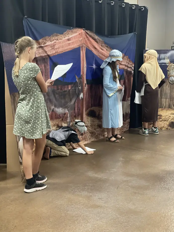 Cornerstone students rehearsing a nativity scene in costume in front of a stable backdrop