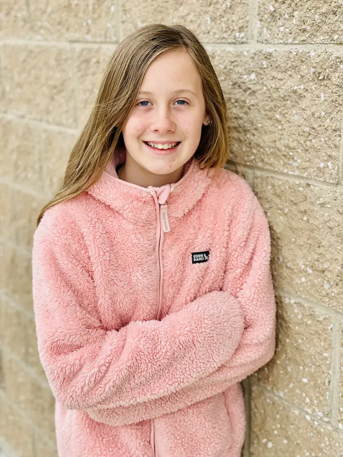 A Cornerstone student smiling with her arms folded outside the school